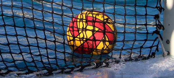 A red and yellow water polo ball floats close to a black net.