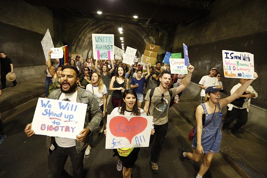 A crowd of protestors march down a tunnel, holding signs that support immigration and put down the Muslim ban.