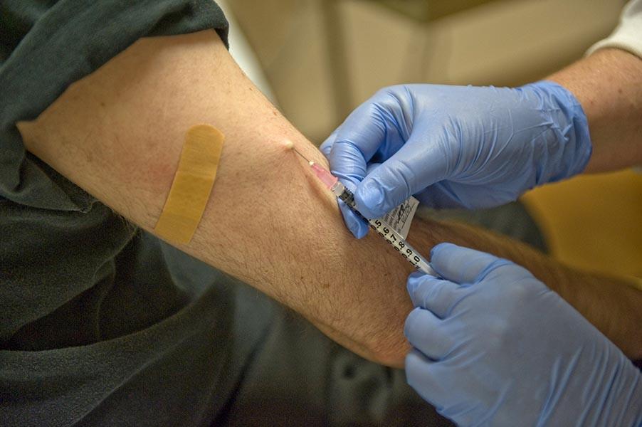 A pair of blue-gloved hands gives someone a shot in the upper arm.