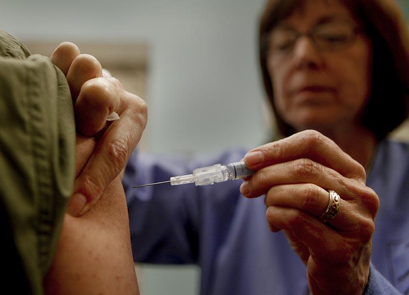 A female nurses gives a shot with a syringe and needle to someone's upper arm.