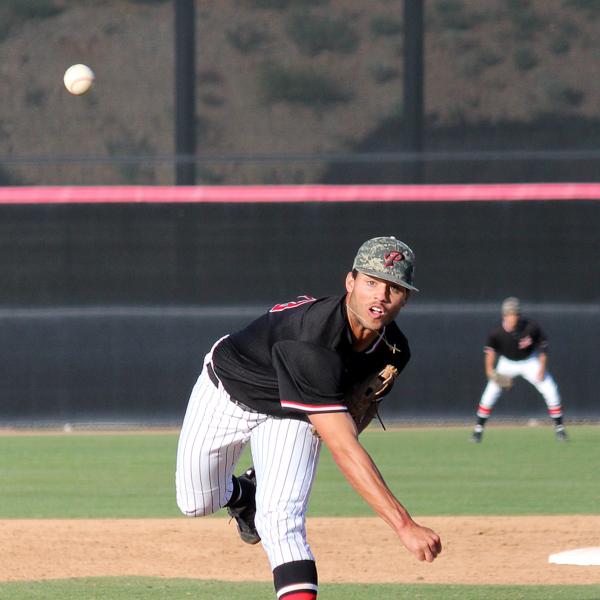 A male Palomar baseball player pitches a baseball (front view). A teammate stands in the background in the outfield.