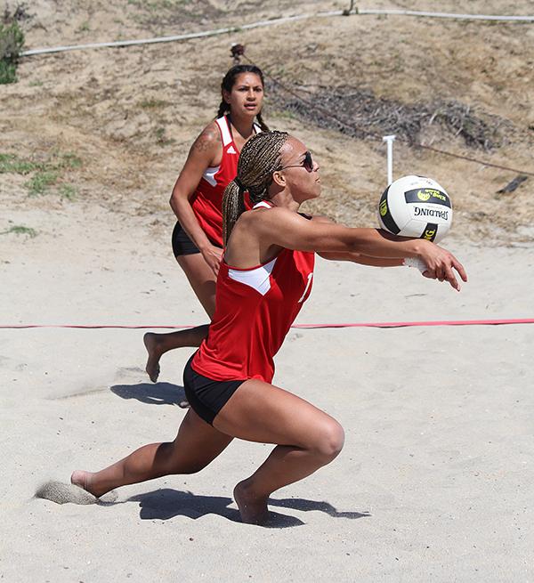 A female Palomar beach volleyball player bumps the ball with her forearms as her teammate looks toward her in the background.