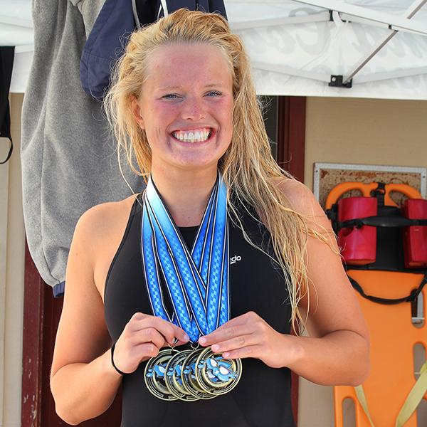 Swimmer Emma Thomas smiles and poses with four medals.