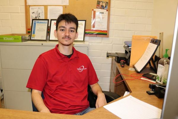 A Palomar student in a red polo shirt sits at a computer desk at Pride Center.