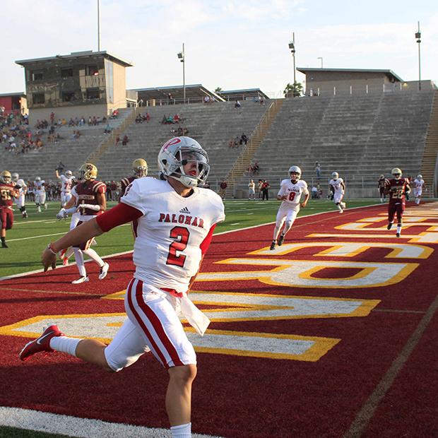 A Palomar football player runs with his arms behind his back. A few players from both teams run and slow down in the background.