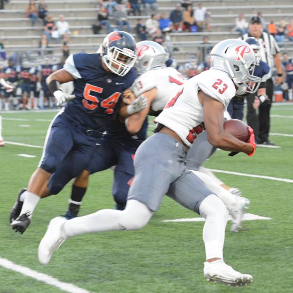 A Palomar football player runs and carries a football in his right arm while a team player tackles two opposing players.