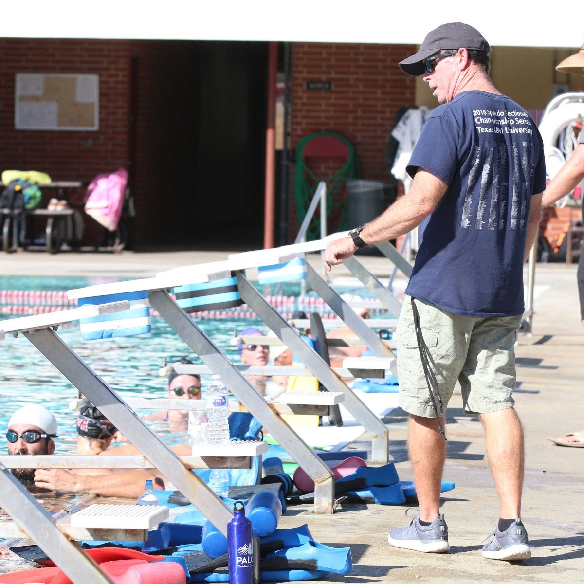 Swim coach Jem McAdams stands by the edge of the pool and speaks to his team of swimmers.