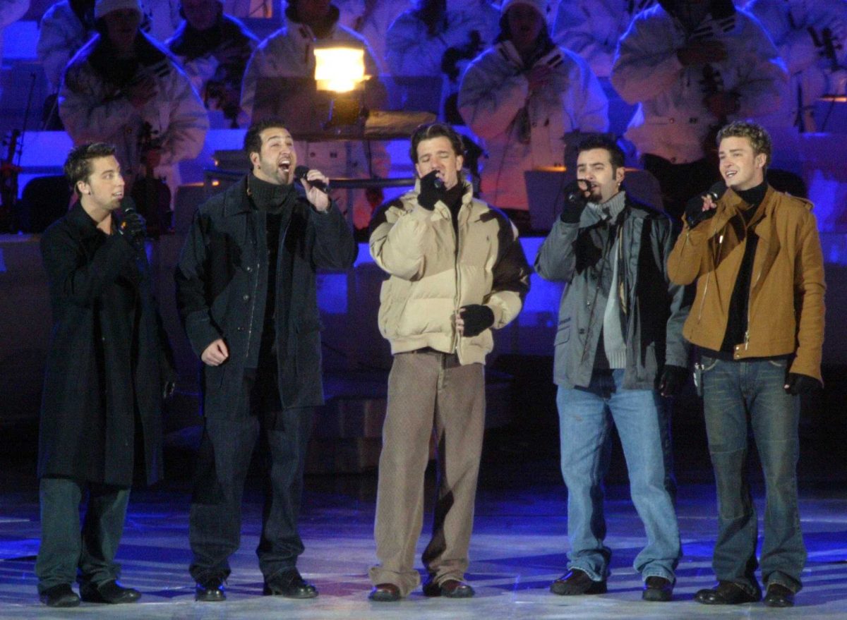 Five members of NSYNC in 2002 sing the National Anthem with a microphone in each of their hands. They all wear winter attire.