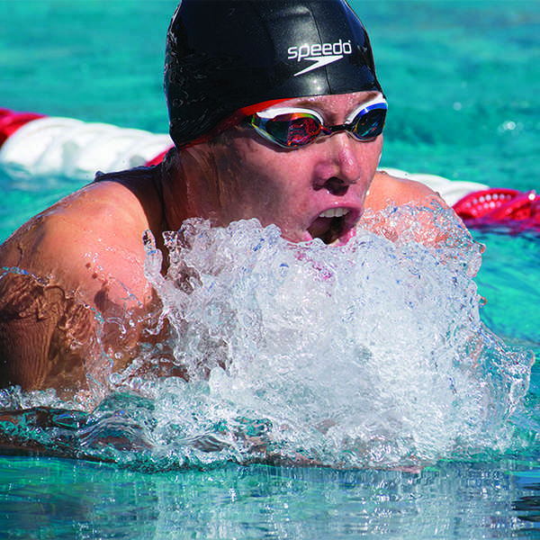 Close up shot of a male Palomar swimmer swimming in a pool, wearing a black swim cap and goggles.