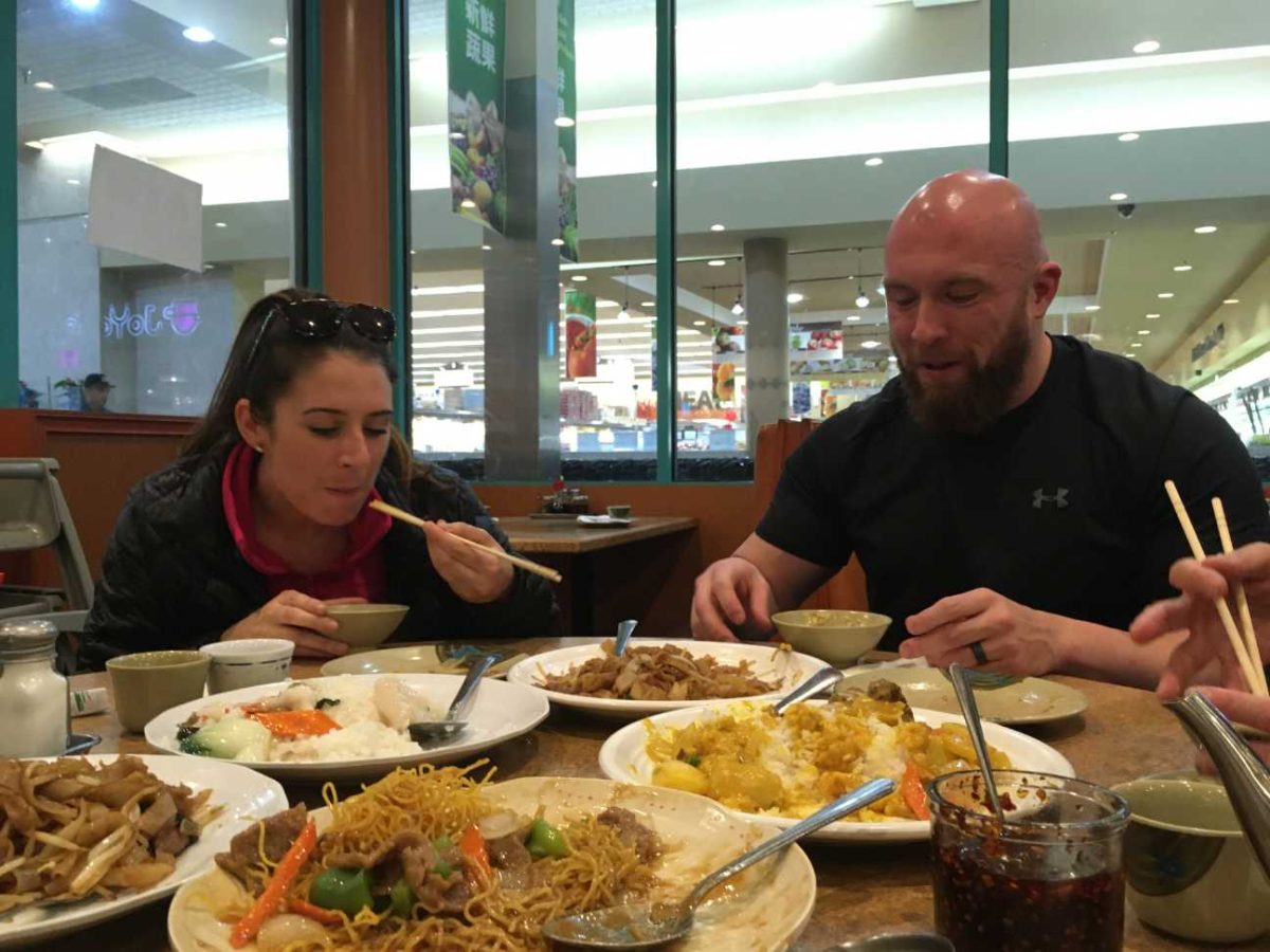 A woman and man eat at a Chinese restaurant with five plates of food in front of them.