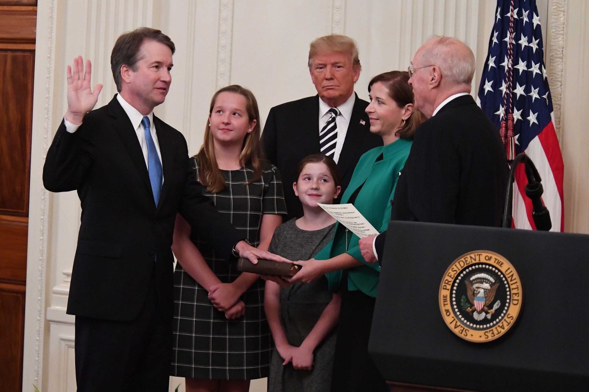 Brett Kavanaugh raise his right hand and put his left hand on a book as he swears an oath. His two daughters and wife, President Donald Trump and Justice A. Kennedy looks on.