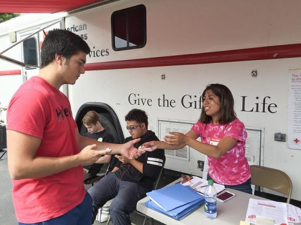 A woman gives a man a sticker outside of a blood drive van.