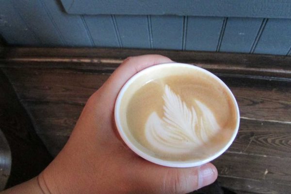 A hand holds a paper cup of umpkin spice latte on a wooden counter.