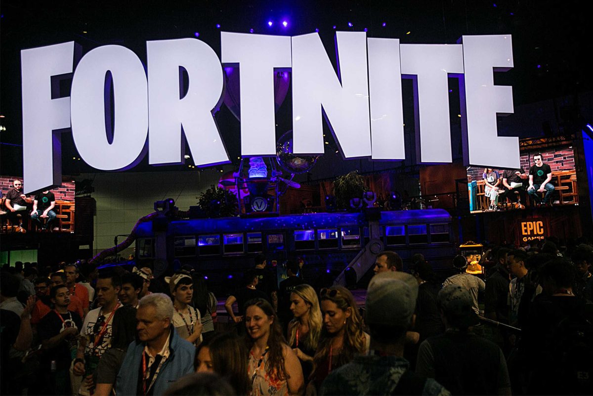 A crowd gathers at an exhibition hall with a huge sign "FORTNITE" hanging from the ceiling.