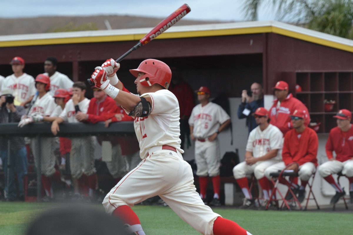 A male Palomar baseball player swings a bat and prepares to run. More than a dozen of his teammates look on from the dugout.