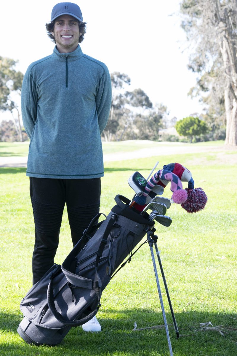 Palomar golfer Jacob Montes stands with his golf bag full of colorful golf clubs on a golf course.