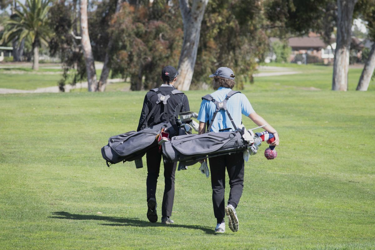 Two Palomar golfers walk on a golf course, carrying their golf bags full of golf clubs and other accessories.