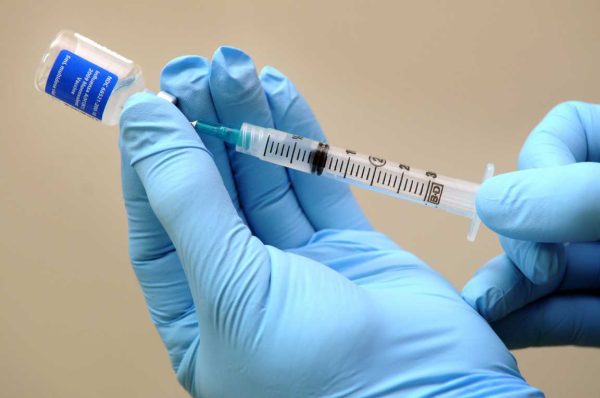 A pair of hands wearing blue gloves draws a vaccine with a syringe.