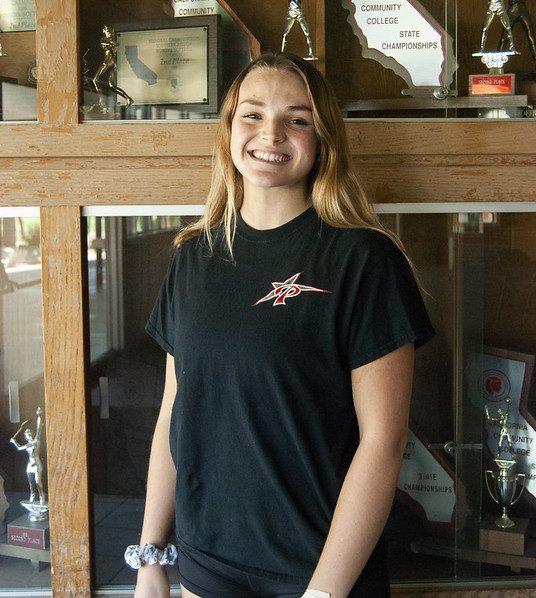 Palomar volleyball player Alina Leakes-Jones smiles and stands near a cabinet full of Palomar College's past trophies.