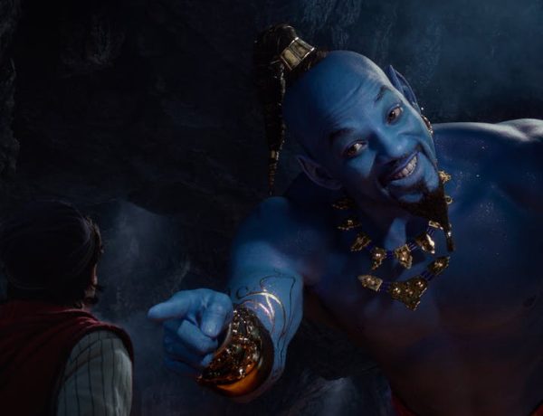 A blue-skin genie who looks like actor Will Smith points and smiles at a man in the lower left, his head turn slightly to his left.