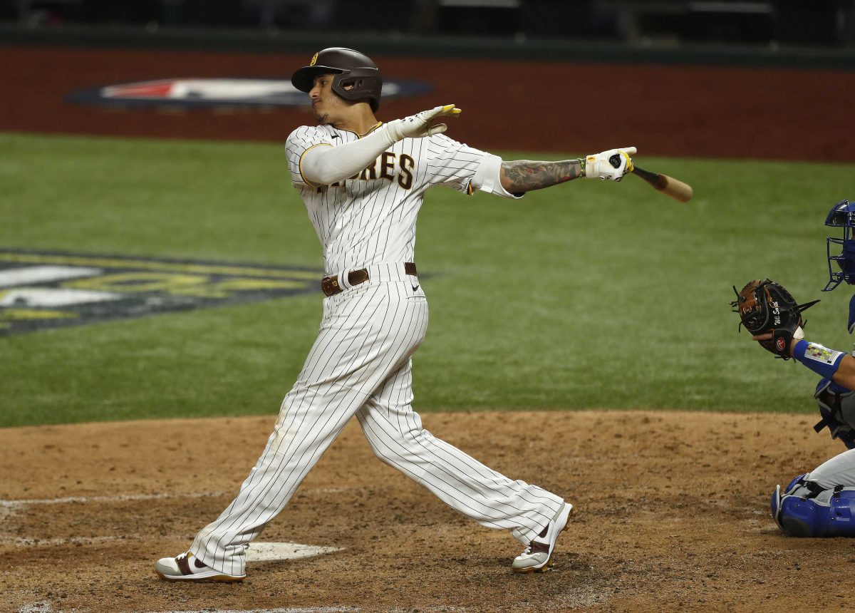 San Diego Padres' Manny Machado swings a bat to his left. A catcher crouches behind him with his mitt ready in front of him.