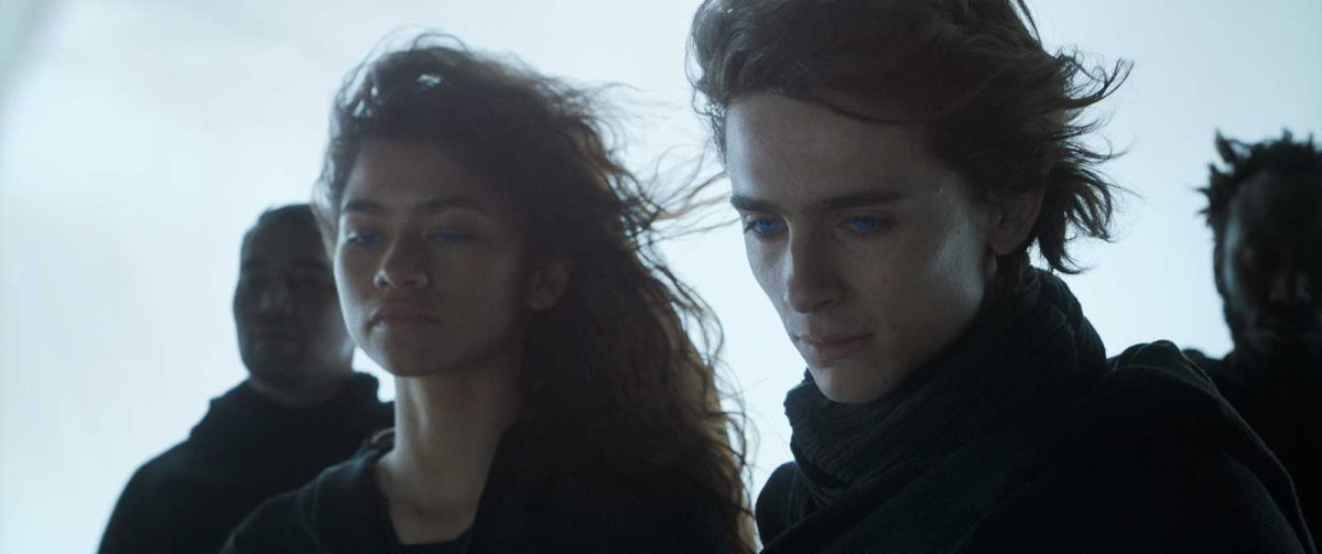 Actors Timothée Chalamet (right) and Zendaya as Paul Atreides and Chani, respectively, in the 2021 movie "Dune." Both are looking at something below them with two men behind them.