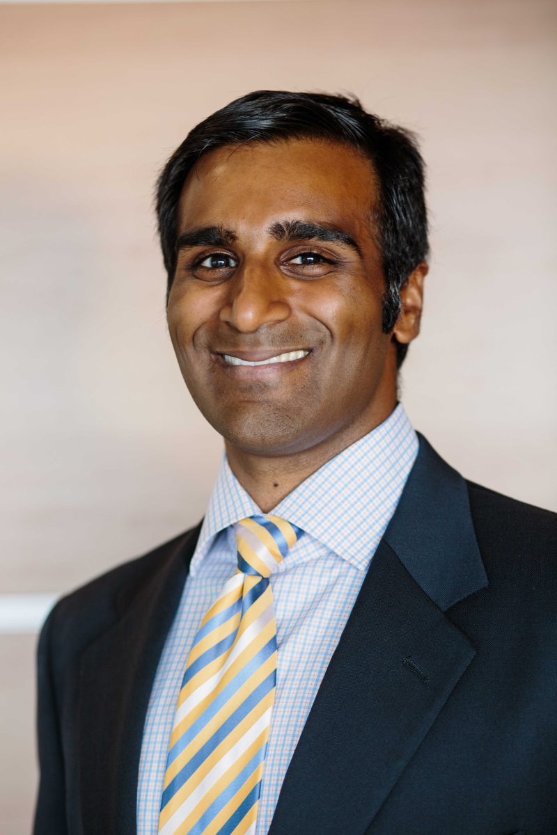 Kartik Raju, Palomar College's New Provisional Trustee, poses and smiles, wearing a blue suit and an orange and blue striped tie.