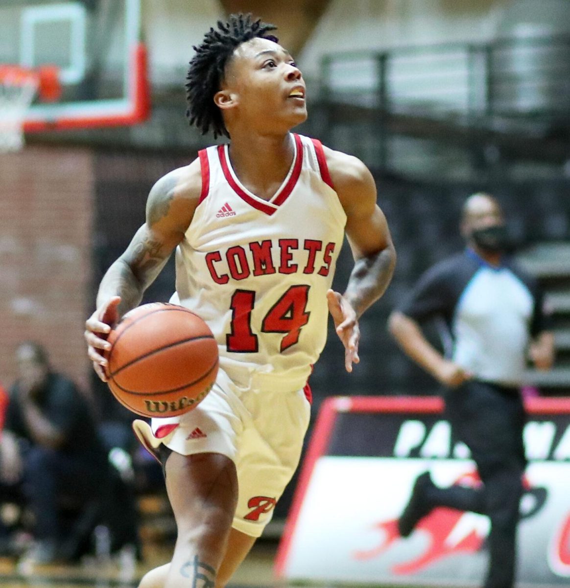 A male Palomar basketball player runs and dribbles a basketball in a court.