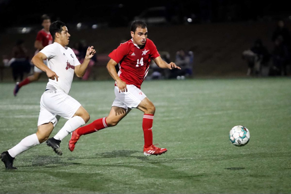 Two soccer players from opposing teams chases after a soccer ball on a field.