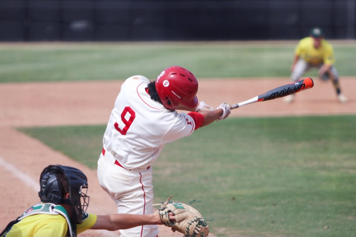 A Palomar baseball players swings a bat with a catcher kneeling next to him.