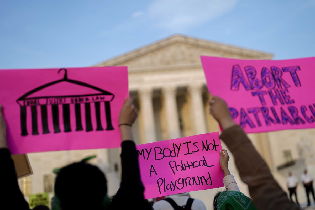 Crowd protesting in front of Supreme Court, holding pink signs.