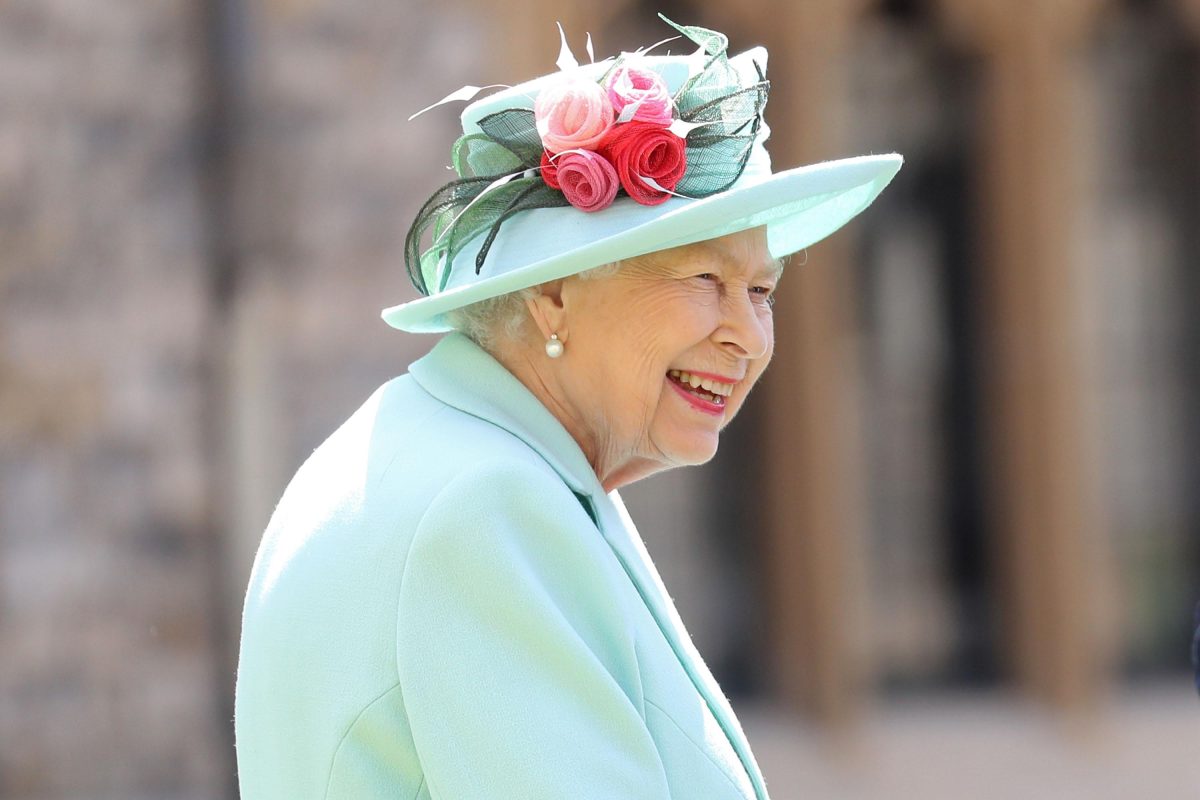 Queen Elizabeth in 2020 wearing a teal hat with pink flowers and a teal coat. She is smiling.