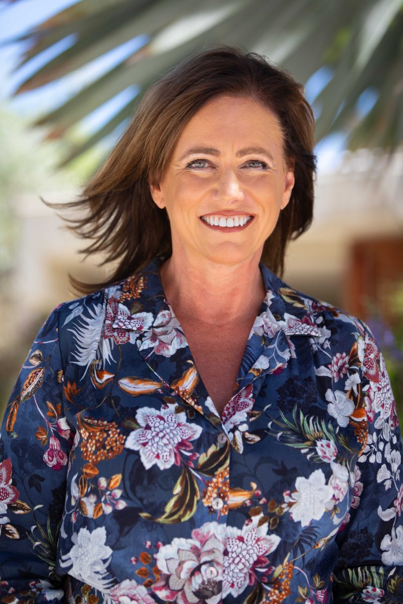 Portrait of a woman smiling, wearing a blue shirt with pink and orange flowery patterns.