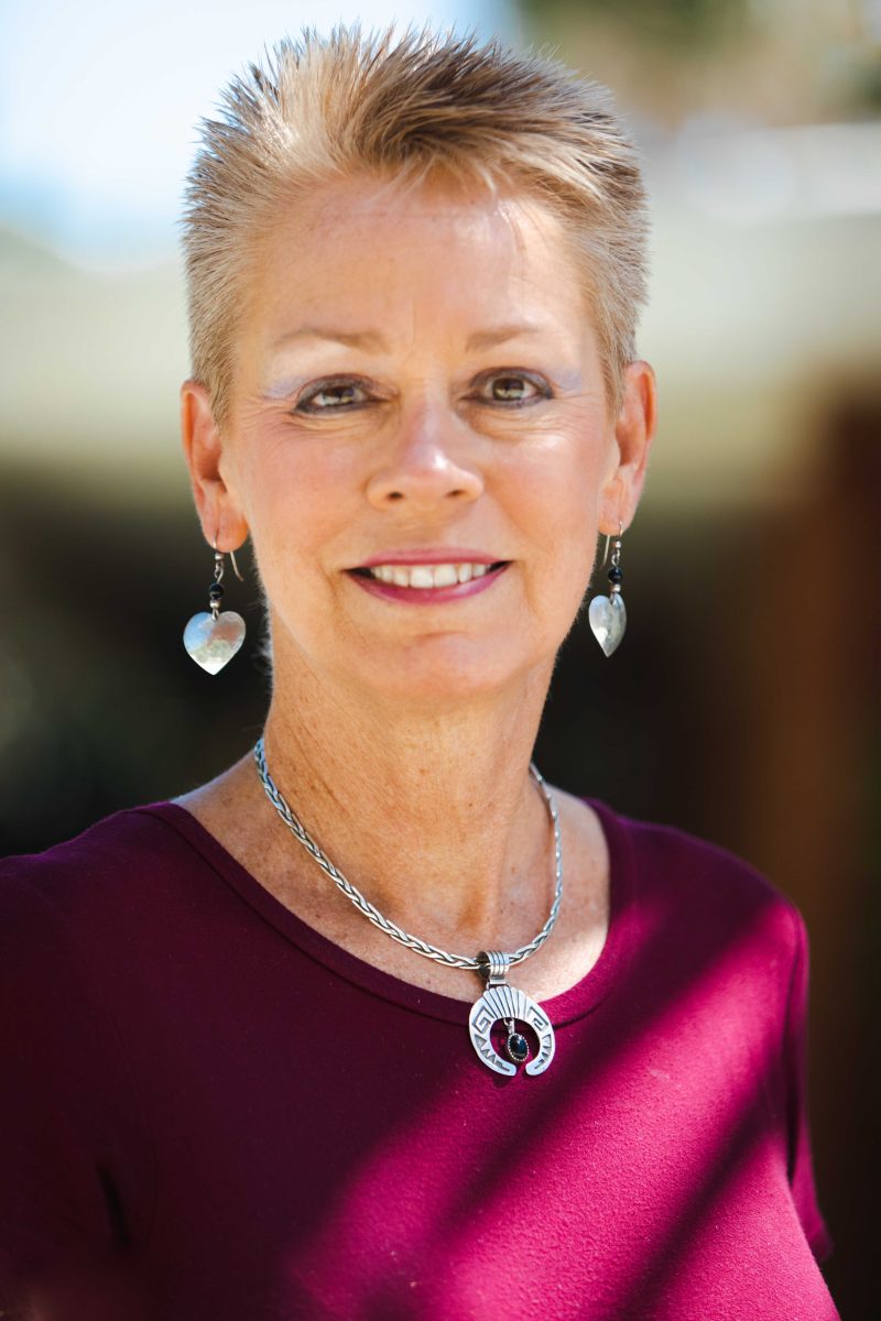 Portrait of a woman with short blonde hair wearing a magenta top and heart-shaped earrings.