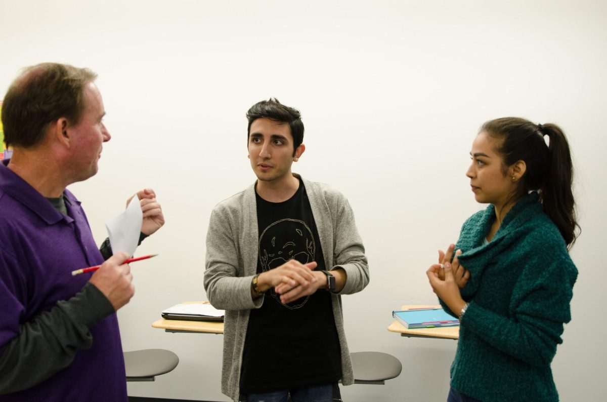 A male and a female Palomar student stand and listen to an instructor speak.