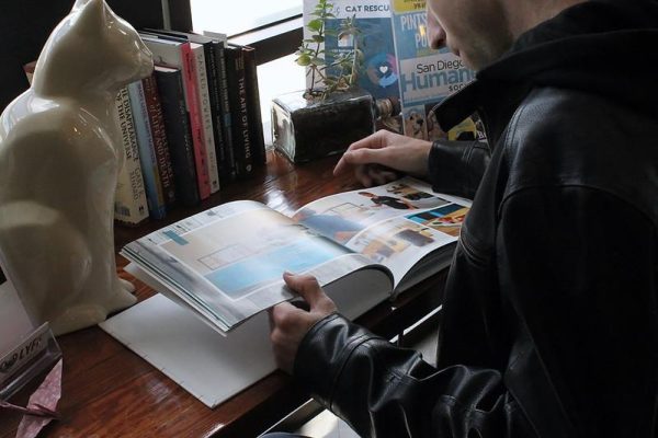 A man reads a large book on a wooden desk.