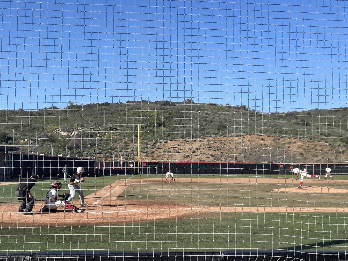 A pitcher throws a baseball as the batter is ready to hit it. A net is in the foreground.