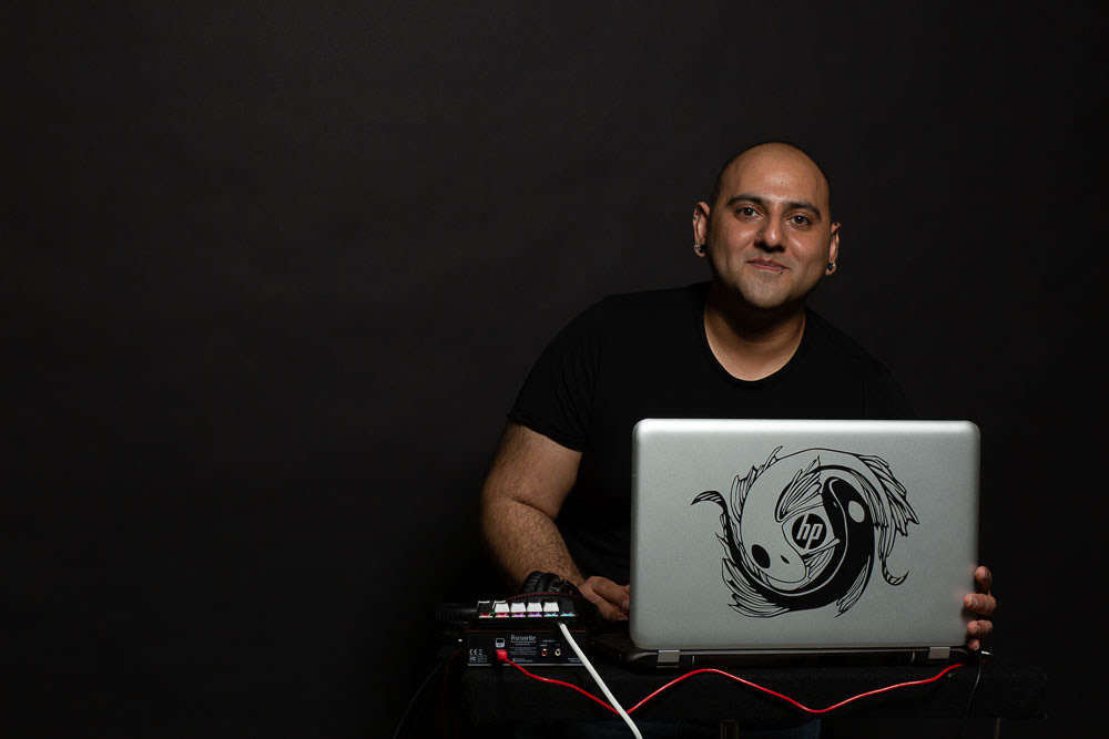 Zeshaun Hassan sits with his laptop and music setup with a black background.