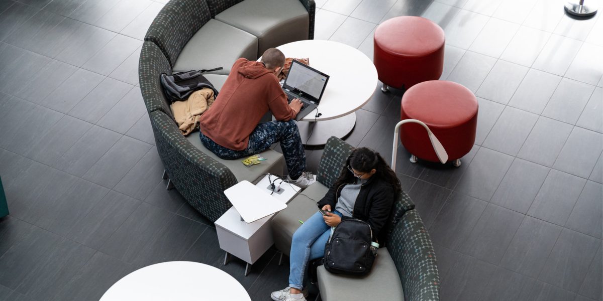 Two students studying on an S-shaped couch at the Palomar College library.