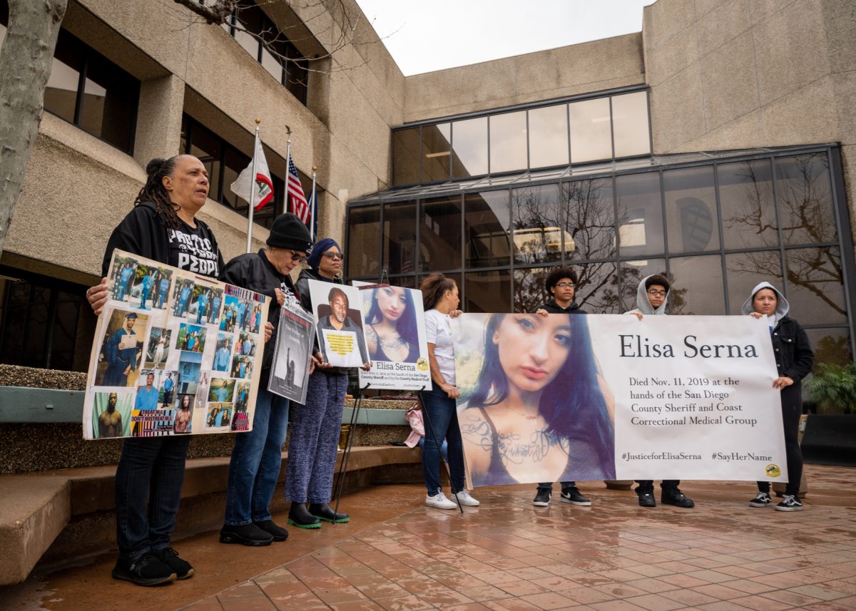 A group of people protests outside of the Escondido Police Department, holding posters and collages of those who died under custody.