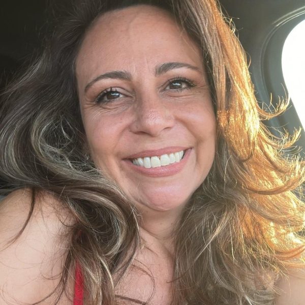 A brunette woman with curly hair smiles at the camera. The sunlight hits the one side of her face.