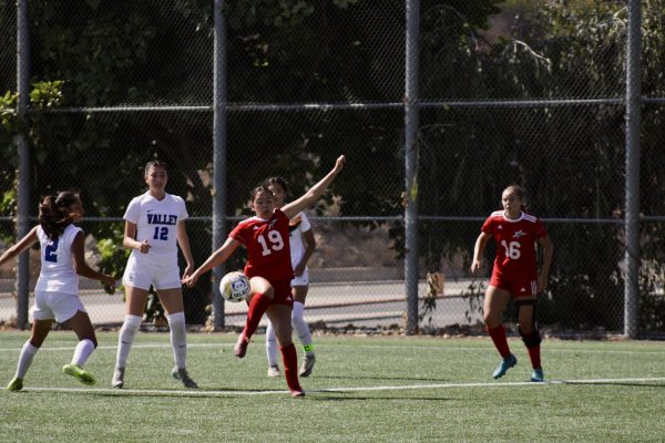 Three players from San Bernardino Valley surround midfielder Eva Lopez as she is lifting her leg to retrieve the ball as it's coming down from the air.