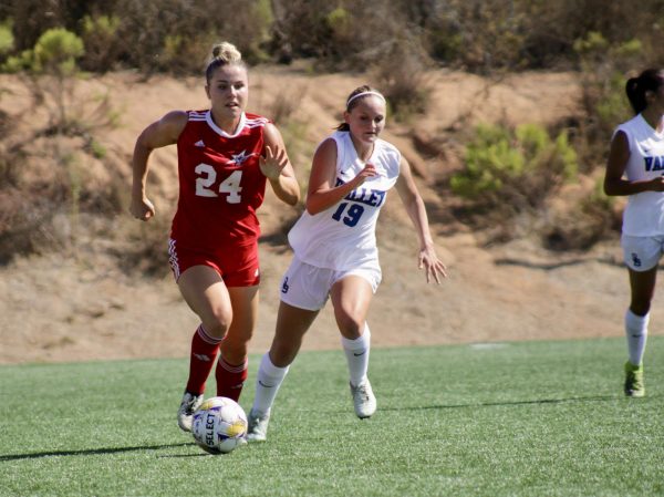 Naomi Allen is dribbling the ball away from Palomar's side of the field while a player from San Bernardino Valley is running closely beside her, trying to take the ball away.
