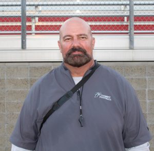 A Palomar football coach in a grey football shirt with a logo reading Comet Football poses for a photo.