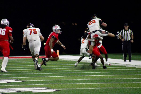 Palomar player in red raises a Ventura player in white into the air as the Ventura player attempts to attempts to hurdle over the Palomar player.