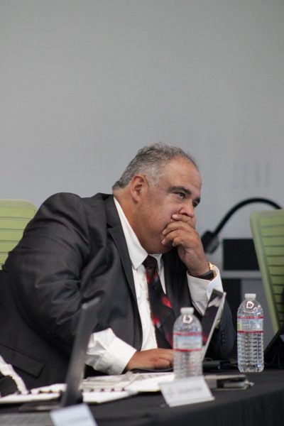 Governing Board Trustee hunched over covering, his mouth during the constituent reports at the September 10, 2025 meeting.
