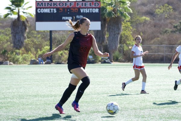 Palomar's Cameryn Doughtery (#20) is running, one arm in front of her and the other behind her, moving with the white and yellow ball down the field to pass it to another player.