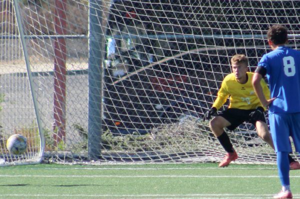Santa Monica number 8 player in blue watches as Palomar player number 26 in yellow sidesteps to his right in reaction to a shot on goal from the penalty area.