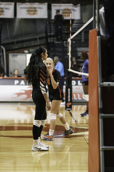 Palomar College's Caden Pinto (#8) has blond hair and is wearing a black and red uniform. She is discussing strategy before a play in the third set with Teiora Tinoisamoa (#6), who is to left of Pinto as the Comets host San Bernardino Valley College on Sept. 10, 2025, at The Dome.