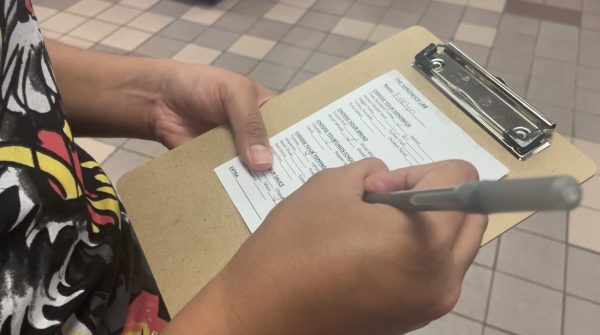 A student hold a clipboard and pen to fill out a small sheet of paper with their order